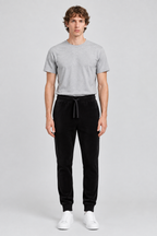 Mannelijk model met de zwarte About You Broek Fernando en een lichtgrijs T-shirt, volledig van voren gefotografeerd
