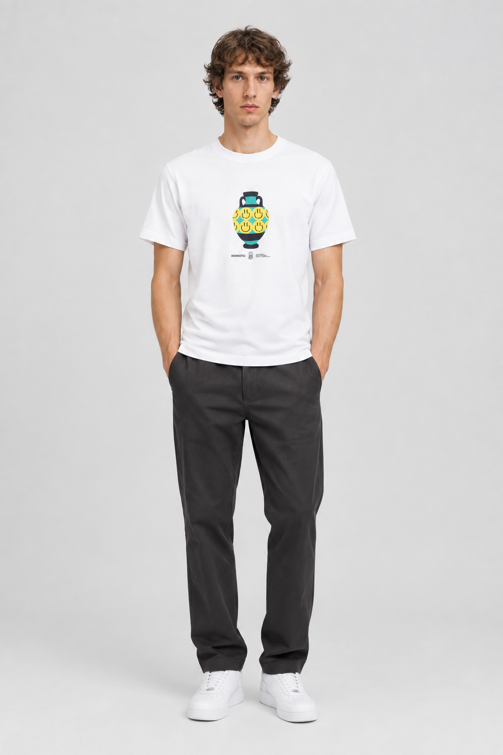 Mannelijk model met het witte Wemoto T-shirt Bruce Vase Tee met kleurrijke vaasprint, volledig van voren gefotografeerd